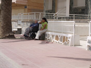 Una anciana descansa con su cuidadora en el paseo de Los Alcázares