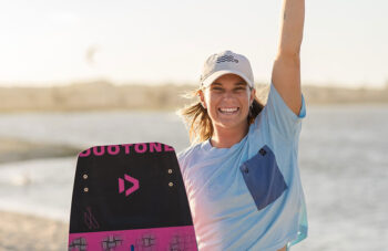 Claudia León sonriente con su tabla de kitesurf en la playa