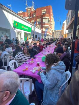 Celebración en la calle con mesas y gente disfrutando de la lotería