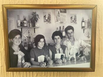 Fotografía en blanco y negro de un bar con cuatro personas detrás de la barra.