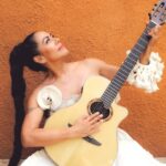 Lila Downs tocando la guitarra con una expresión de alegría