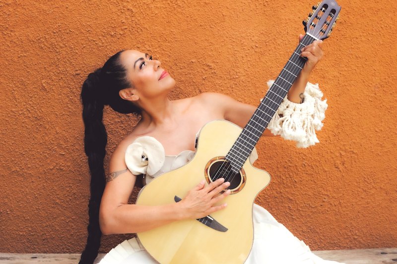 Lila Downs tocando la guitarra con una expresión de alegría