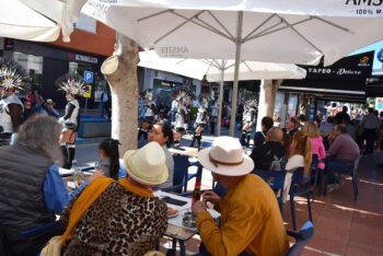 Familias disfrutando del carnaval en una terraza con comparsas desfilando.