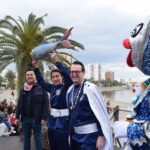 Tres personas sosteniendo una sardina en un evento festivo en Santiago de la Ribera.