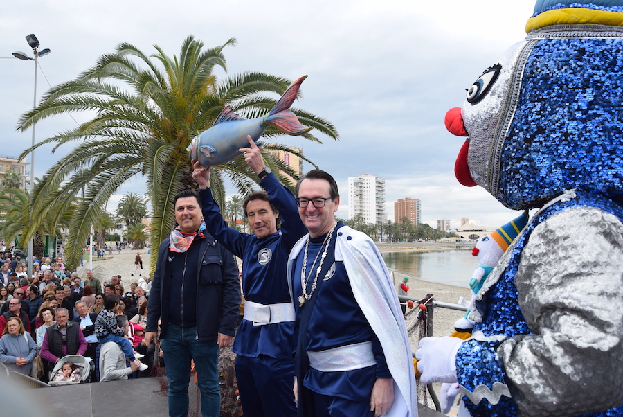 Tres personas sosteniendo una sardina en un evento festivo en Santiago de la Ribera.