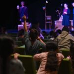 Niños en el teatro levantando la mano durante una representación