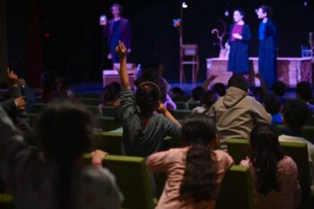 Niños en el teatro levantando la mano durante una representación