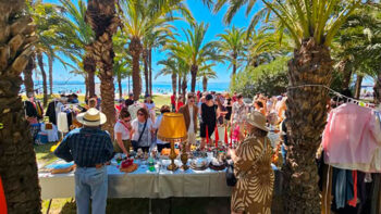 Vista de un mercadillo al aire libre con palmeras y gente comprando.