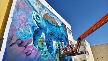 Mural de una tortuga marina pintado en una fachada durante un festival de arte urbano.