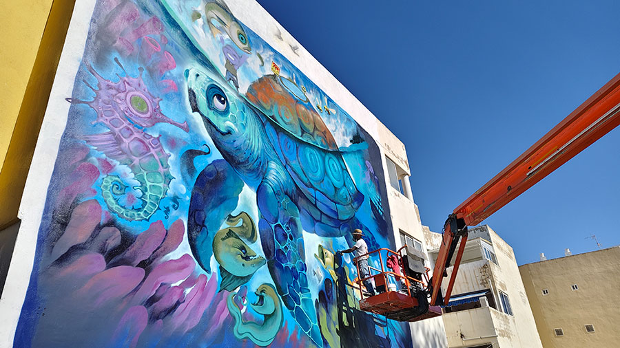 Mural de una tortuga marina pintado en una fachada durante un festival de arte urbano.