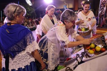 Mujeres en trajes tradicionales preparando ofrenda de frutas