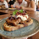 Montadito servido en un plato en un bar con comensales al fondo