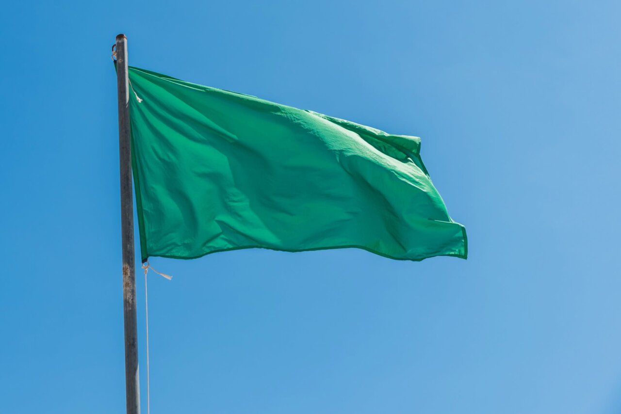 Bandera verde ondeando en la playa de Los Narejos bajo un cielo azul