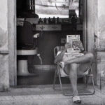 Persona leyendo una revista en la entrada de un bar en Torre Pacheco