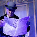 Actor leyendo un periódico en una obra de teatro de Agatha Christie.