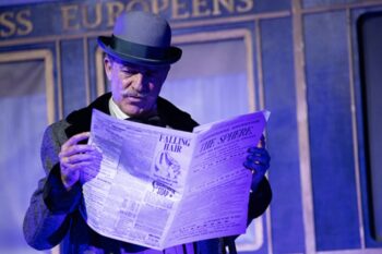 Actor leyendo un periódico en una obra de teatro de Agatha Christie.