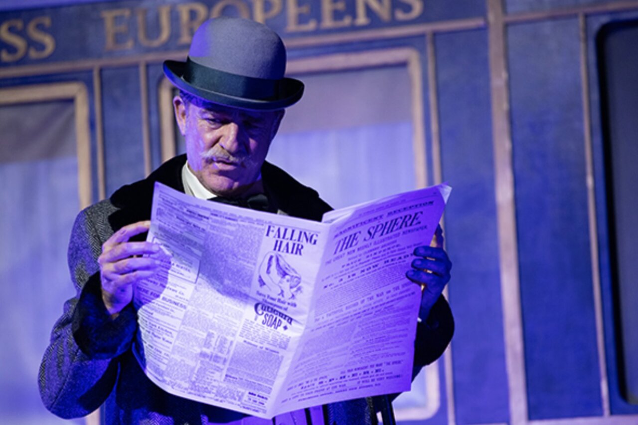 Actor leyendo un periódico en una obra de teatro de Agatha Christie.